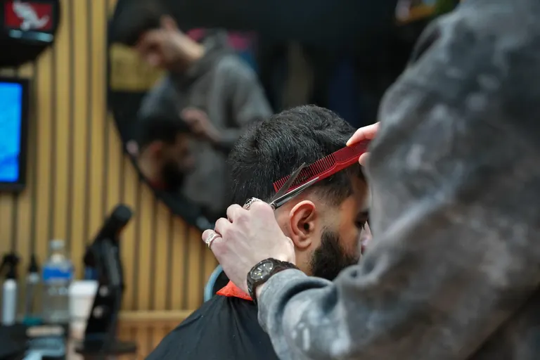 AB Barbers, Putney. A barber runs a red comb through a customer's hair.