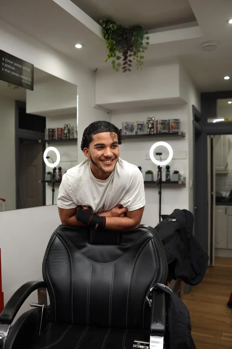 Another Level Barbers, Anerley. A barber leans on the chair, smiling.