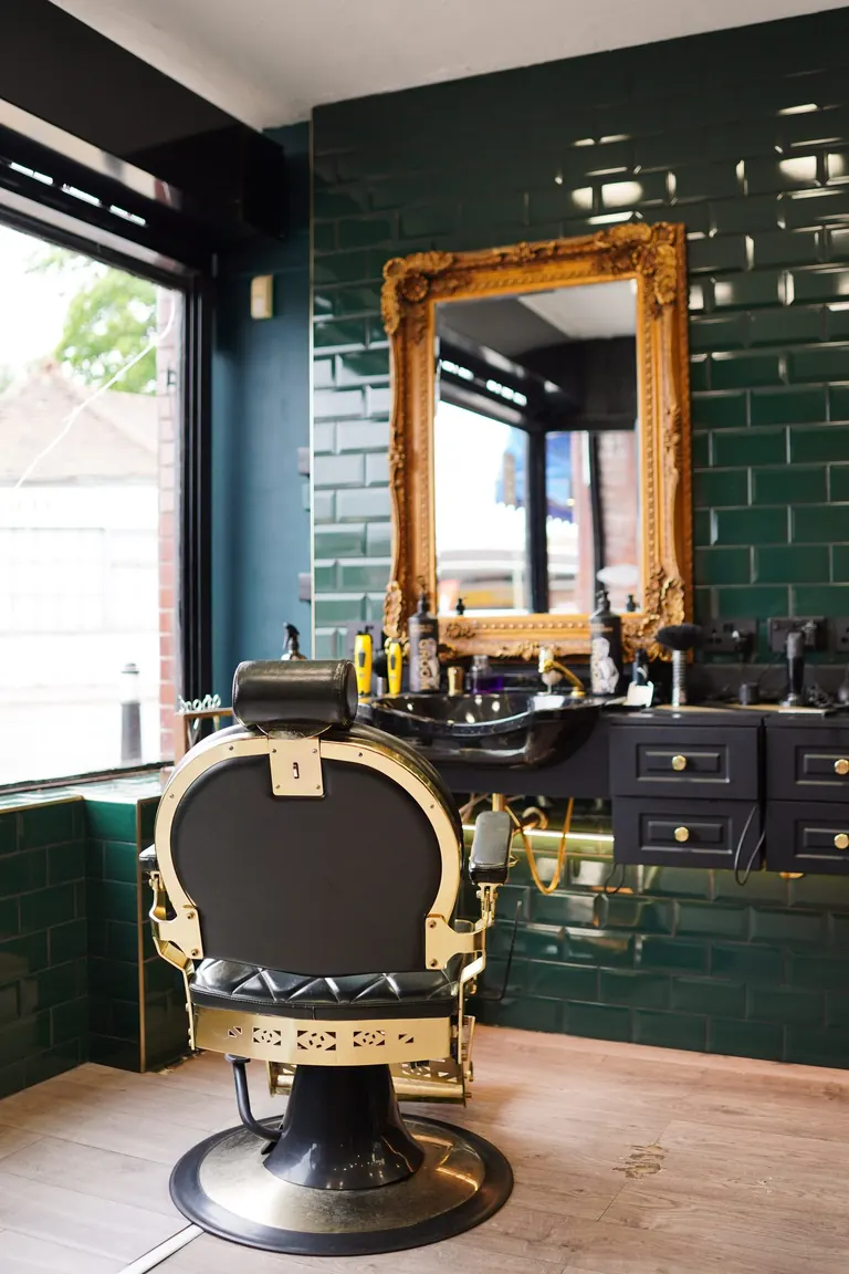 Groom Barbers, Lingfield, Surrey. A barber chair in front of green tiles and a gilt mirror.