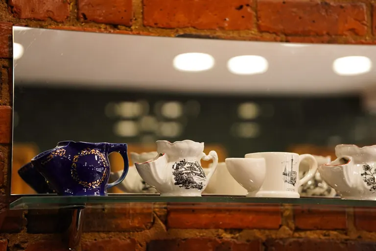 Groom Barbers, Lingfield, Surrey. Shaving mugs on a glass shelf against brick.