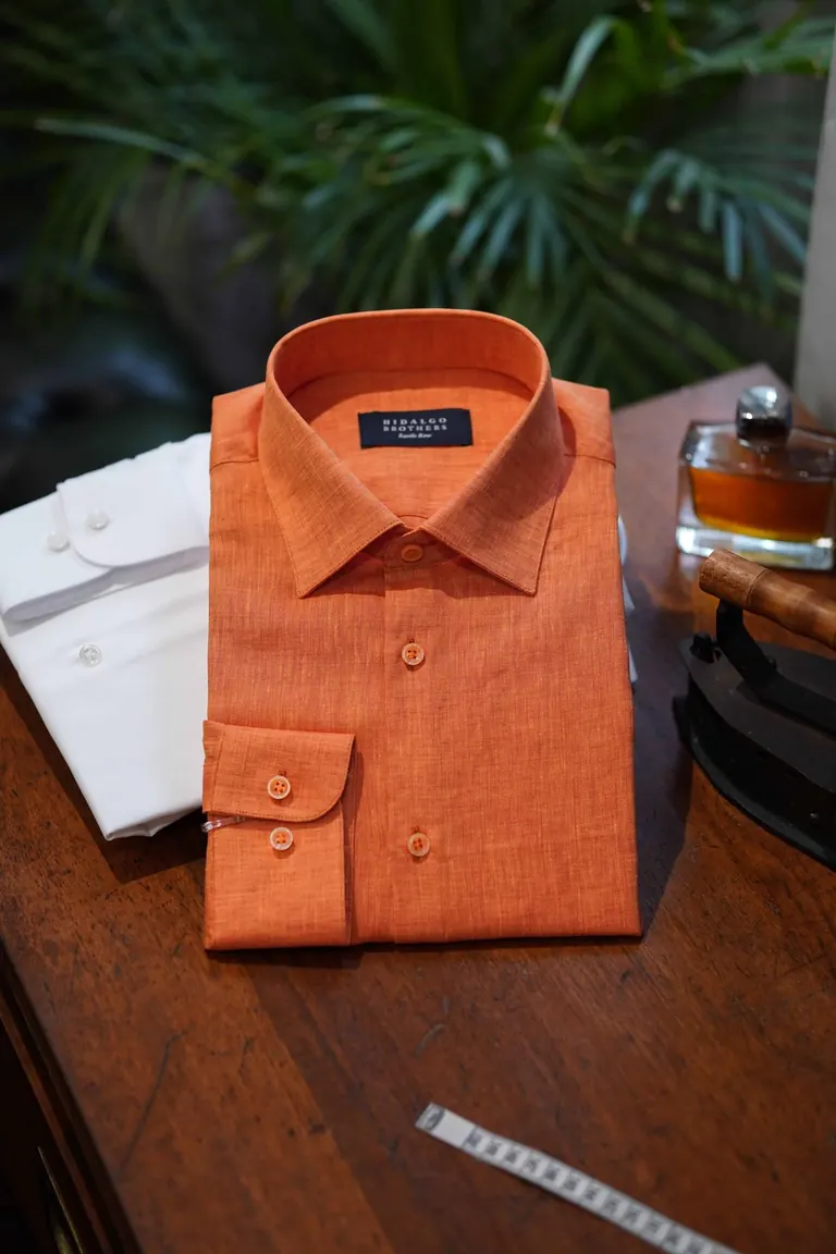 Hidalgo Brothers, Savile Row, London. A folded orange shirt on a wooden table, tape measure beside it.