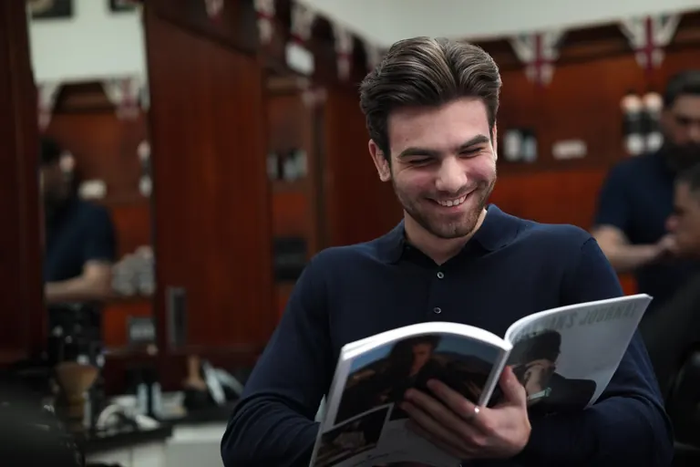 Pall Mall Barbers, London. A customer laughs over a magazine while he waits.