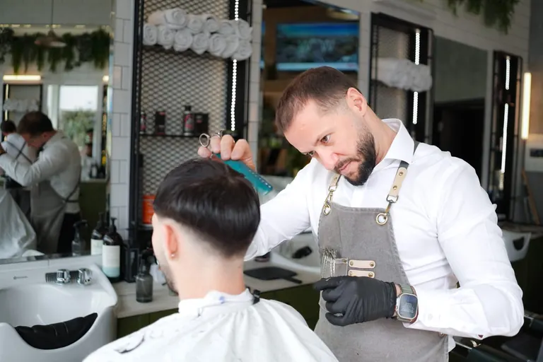 The Axe Club, London. An Axe Club barber combs through a taper in the bright shop.