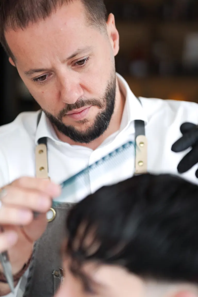 The Axe Club, London. The barber combs through a fringe, gloves on.