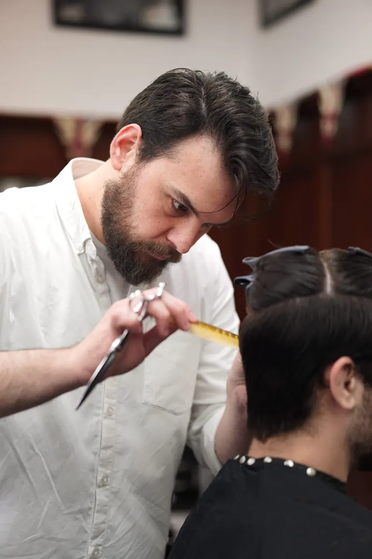A barber at Pall Mall Barbers cutting with scissors and a comb.